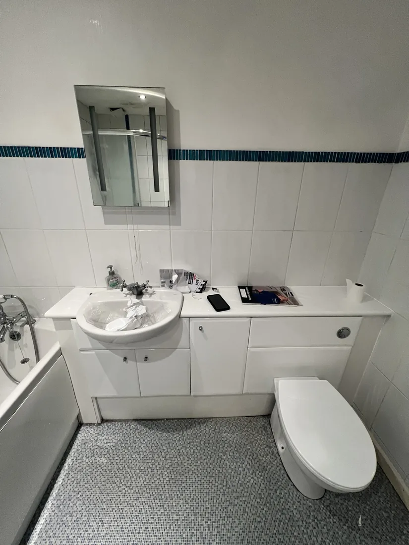 The same bathroom before renovation — dated white units and worn tiling